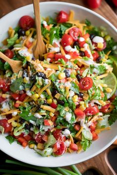 a salad with corn, tomatoes, lettuce and black olives in a white bowl