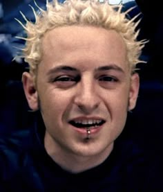 a man with blonde hair and piercings on his face is smiling at the camera