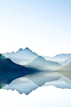 the mountains are reflected in the still water on the lake's surface as it is foggy