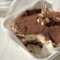 a piece of cake in a container with a teddy bear decoration on the top and chocolate frosting