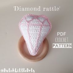 a crocheted white and pink heart sitting on top of a wooden ring holder