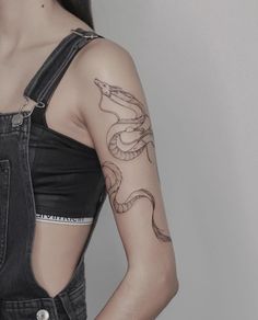 a woman with a snake tattoo on her arm and shoulder, standing in front of a white wall