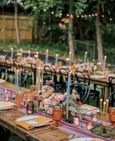 a long table with candles and flowers on it is set up for an outdoor dinner