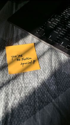 a sticky note sitting on top of a bed next to a laptop