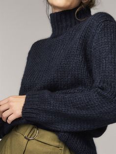 a woman wearing a turtle neck sweater and khaki pants with her hands on her hips