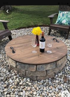 an outdoor table with two wine glasses and bottles on it, surrounded by graveled stones