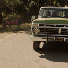 an old green truck driving down a dirt road next to a sign that says beware