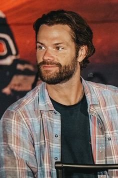 a man with a beard sitting in front of a microphone and looking off to the side