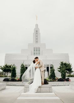 a bride and groom kissing in front of the mormon temple on their wedding day, with veil blowing in the wind