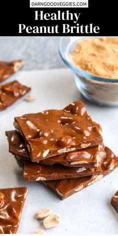 chocolate peanut brittles stacked on top of each other with peanuts scattered around the edges