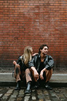 a man and woman sitting next to each other in front of a brick wall