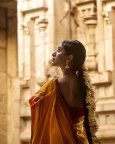 a woman in an orange and yellow sari with flowers on her head looking off into the distance