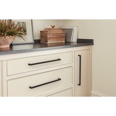 a white dresser with black handles and some books on it's top shelf next to a potted plant