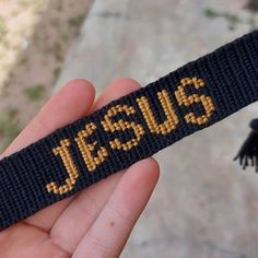 a hand holding a black wristband with the word jesus on it and a tassel