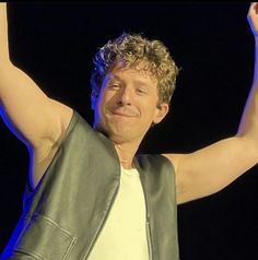 a man with his arms up in the air and wearing a leather jacket on stage