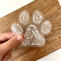 a person is holding an animal's paw shaped sticker on a wooden surface