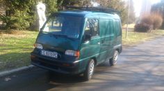 a green van is parked on the side of the road in front of a statue