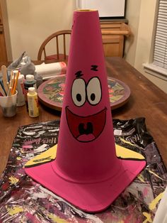 a pink cone sitting on top of a wooden table next to a plate with an angry face drawn on it