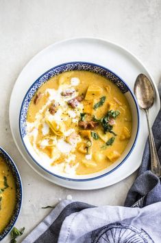 two bowls of soup on a table with silver spoons and blue napkin next to it