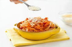 someone is sprinkling parmesan cheese on top of spaghetti in a yellow bowl