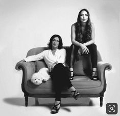 two women sitting on top of a couch with a white dog in front of them