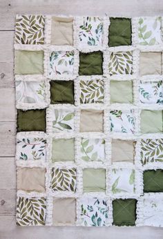 a green and white quilted wall hanging on the side of a wooden floor with leaves