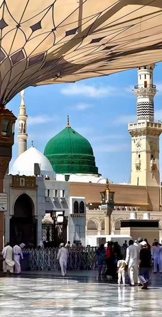 many people are walking around in front of some buildings with green domes and white walls