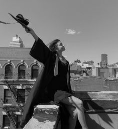 a woman sitting on top of a building holding a hat