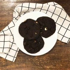 three chocolate cookies on a white plate with a black and white checkered cloth next to it