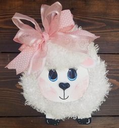 a white sheep with a pink bow on it's head sitting on a wooden surface