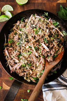 a skillet filled with meat and vegetables on top of a wooden table next to sliced limes