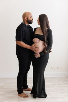 a pregnant woman and man standing next to each other in front of a white wall