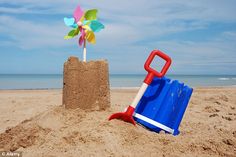 a blue and red beach chair sitting in the sand next to a toy windmill on top of a sandy beach