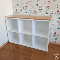 a white bookcase with wooden top in front of a colorful wallpaper