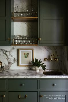 a kitchen with green cabinets and marble counter tops, gold pulls on the cupboards