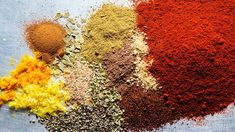 several different types of spices are shown on a blue tablecloth with an orange, yellow and red color scheme