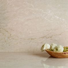 some white flowers in a wooden bowl on a marble counter top with a light colored wall behind it