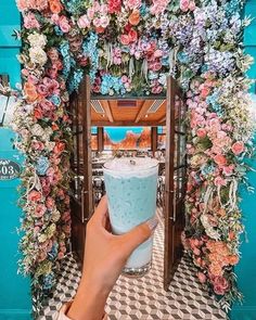 a person holding up a drink in front of a blue wall with flowers on it