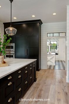 a large kitchen with black cabinets and white counter tops, wood flooring and an island