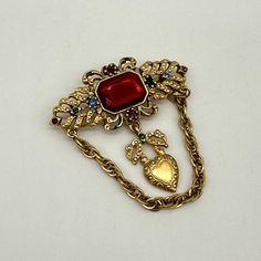 Victorian Style Glass Red Jeweled Gold Toned Brooch Pin Womens Chain Detail. This is an eye-catching brooch. It is gold toned metal with glass rhinestones. It has a dangling heart and chain. It is in good vintage condition. Please see the pictures for the full description. Vintage Red Pins For Party, Red Retro Brooch Jewelry, Retro Red Brooch Jewelry, Vintage Gold Brooches With Jewels, Red Jewel, Victorian Style, Victorian Fashion, Gold Tone Metal, Brooch Pin