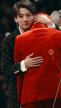 a man in a red jacket hugging another man's back on the catwalk