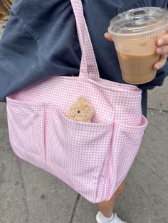 a person holding a pink bag with a teddy bear in it and a cup of coffee