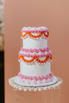 a three tiered cake with pink, orange and white icing on a stand