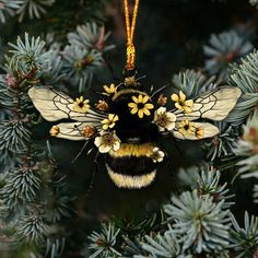 a yellow and black bee ornament hanging from a pine tree with flowers on it