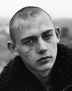 black and white photograph of a man with shaved hair wearing a jacket looking at the camera