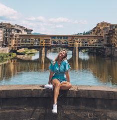 a woman sitting on the edge of a wall next to a river