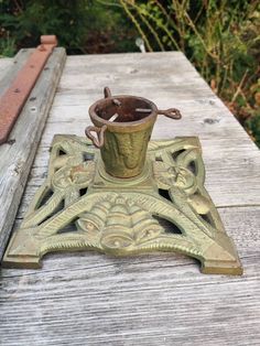 an old fashioned metal cup and saucer sitting on a wooden table in front of some bushes