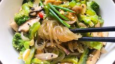 a white bowl filled with noodles, broccoli and other vegtables