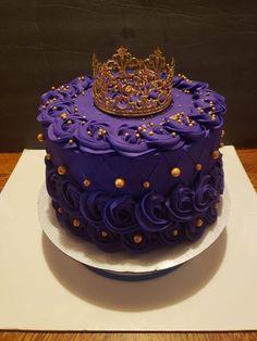 a purple cake with gold decorations and a crown on top is sitting on a white plate