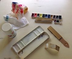 an assortment of art supplies including paint, brushes and paper on a white table top